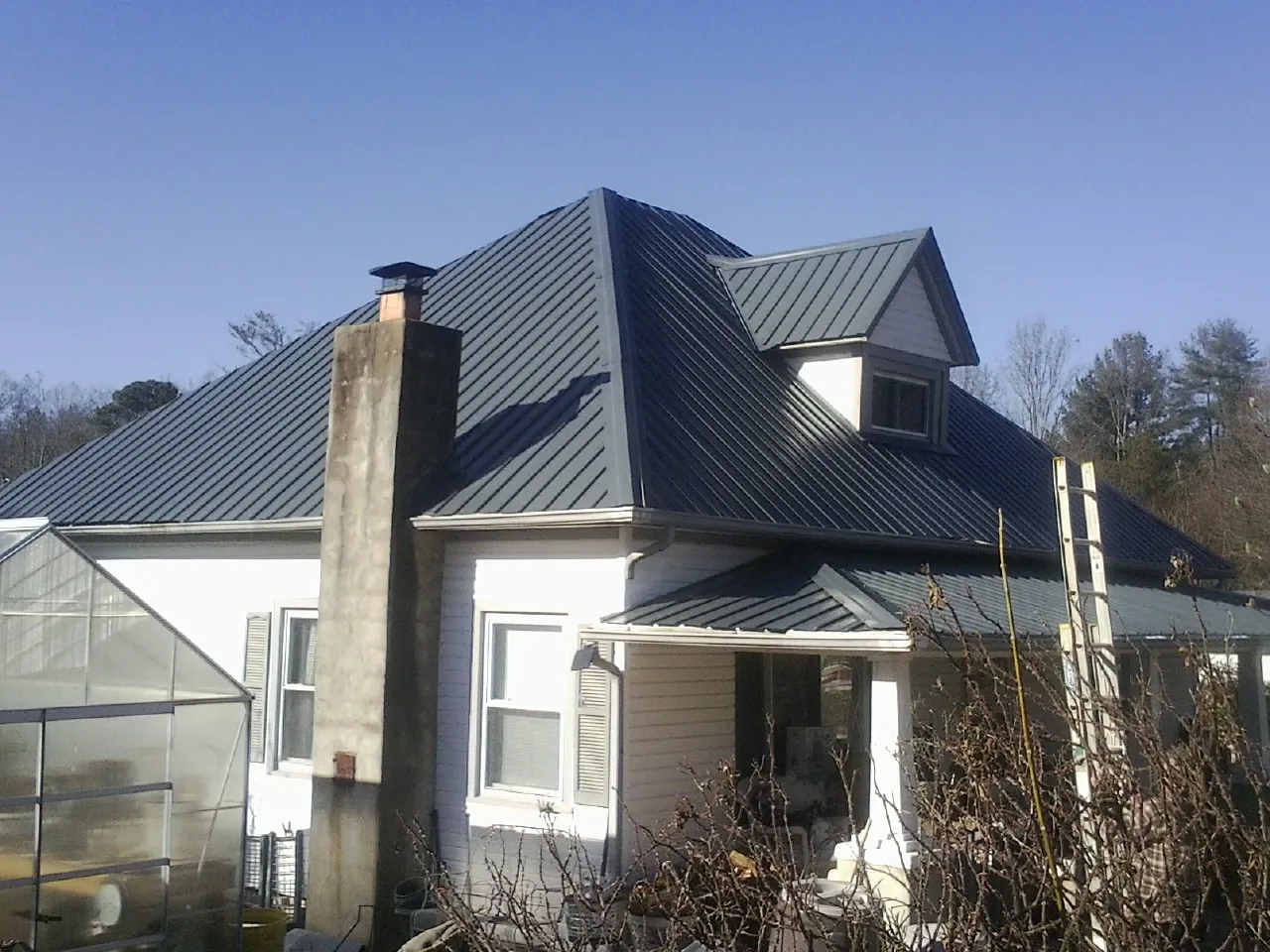 Dark blue standing seam metal roof on a white farmhouse with dormer — Slate & Tile Roof Repair by Roofing Brothers in Andrews Air Force Base