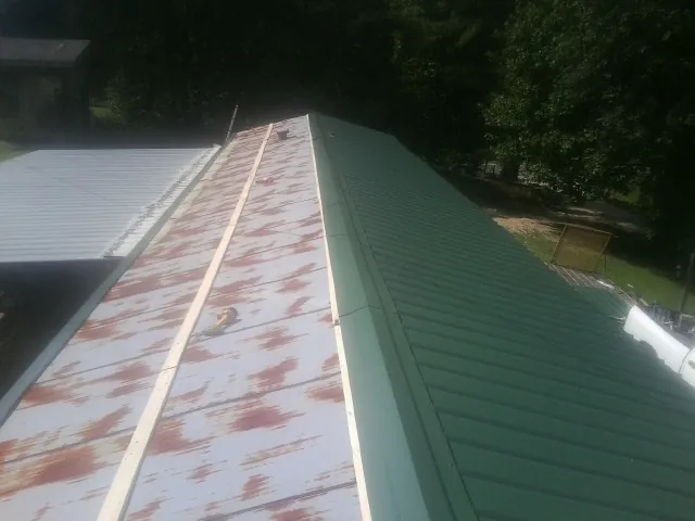 Old rusted panels beside newly installed green metal roofing — Wind Damage Roof Repair by Roofing Brothers in Andrews Air Force Base