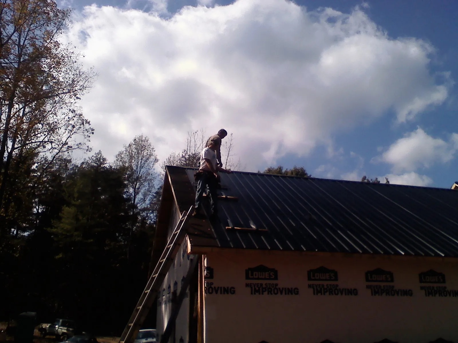 Roofer fastening dark metal panels high against a cloudy sky, from a Roof Inspection job in Andrews Air Force Base