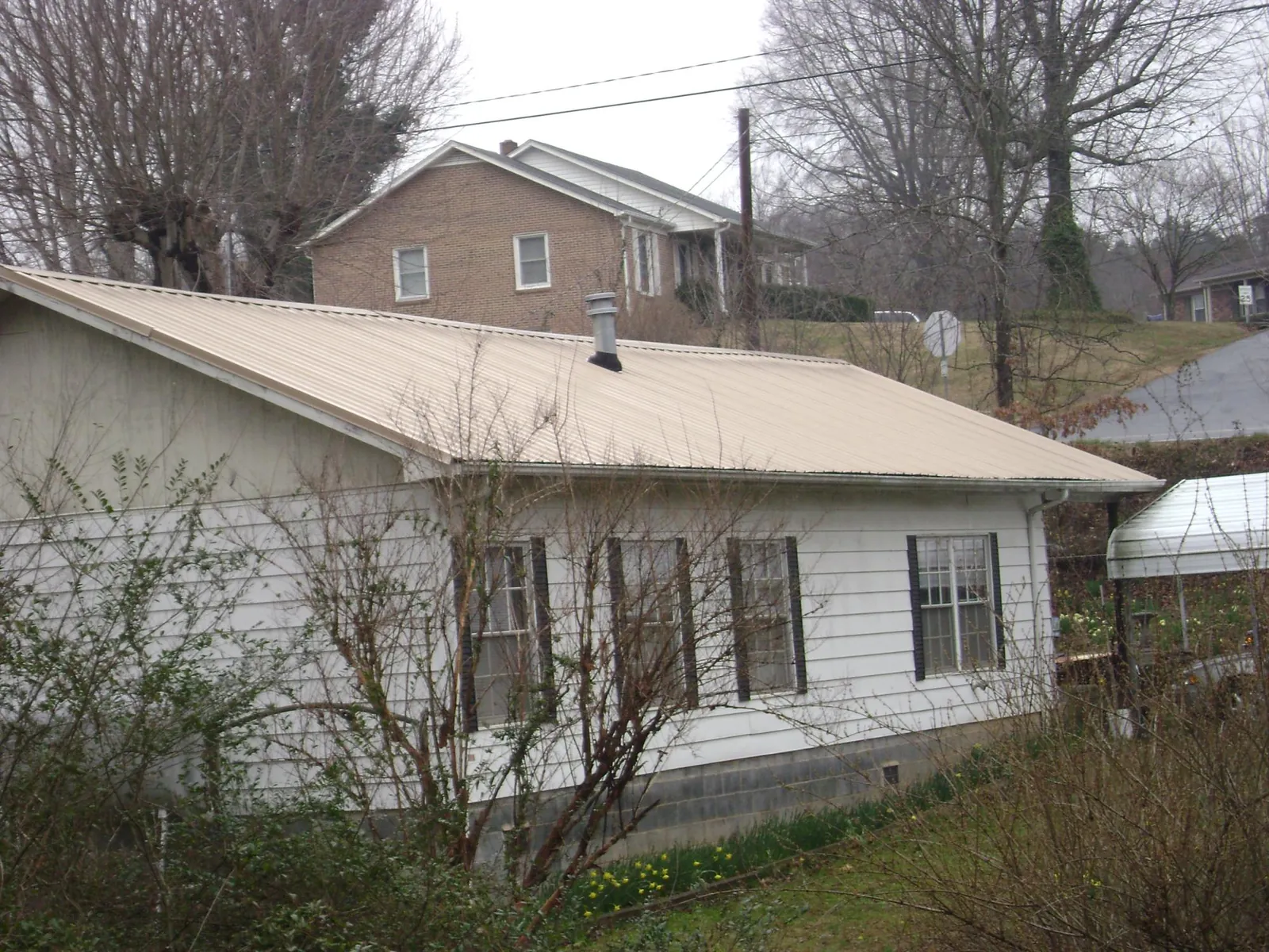 Tan metal roof on a white sided house set into a hillside — Commercial Roofing by Roofing Brothers in Andrews Air Force Base